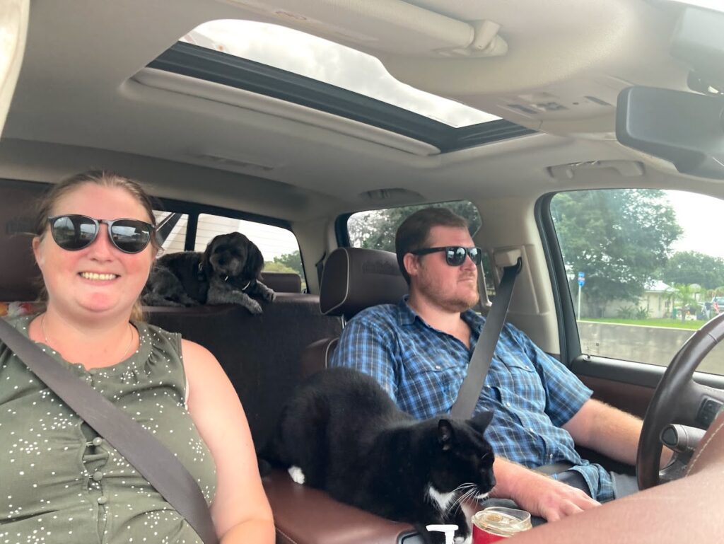 Couple with cat and dog sitting inside truck towing RV on road trip.