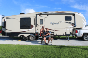 Family posing on picnic table at RV campsite.