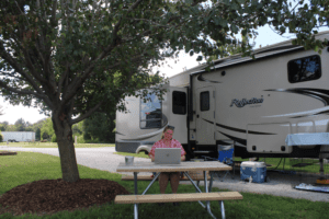 Woman working on computer at picnic table outside RV.