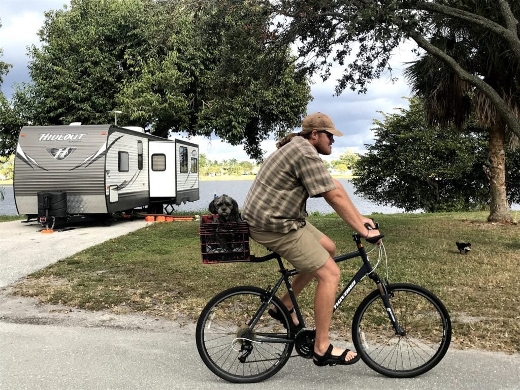 Man biking through campground with dog in basket