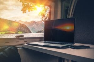 Laptop on table inside RV by window with scenic view.