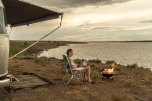 Man working on computer by water outside of Airstream RV.