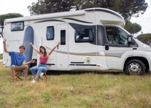 Couple with arms in the air sitting outside a Class C RV.