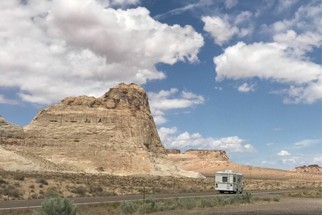 Class C RV driving down road beside limestone formations.