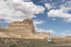 Class C RV driving down road past rock formations.