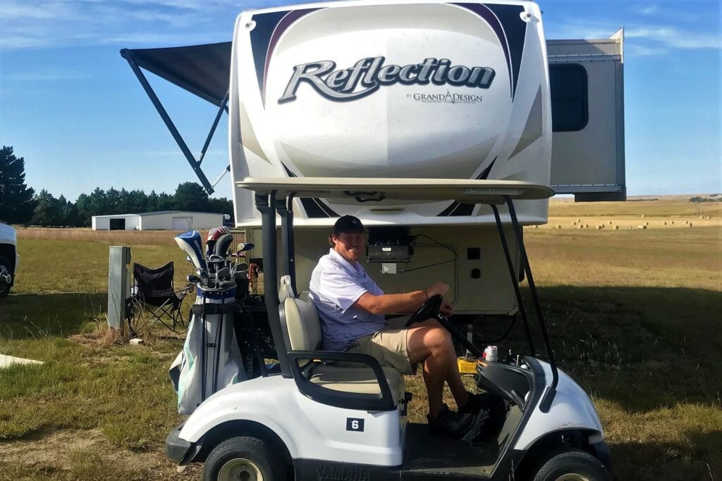 Man on golf cart parked in front of fifth wheel RV.