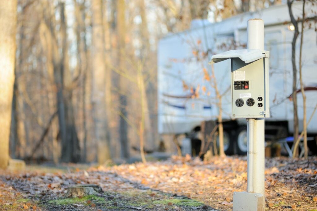 Power pole next to RV parked in woods.