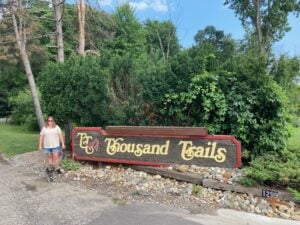 Woman standing in front of Thousand Trails RV park sign.