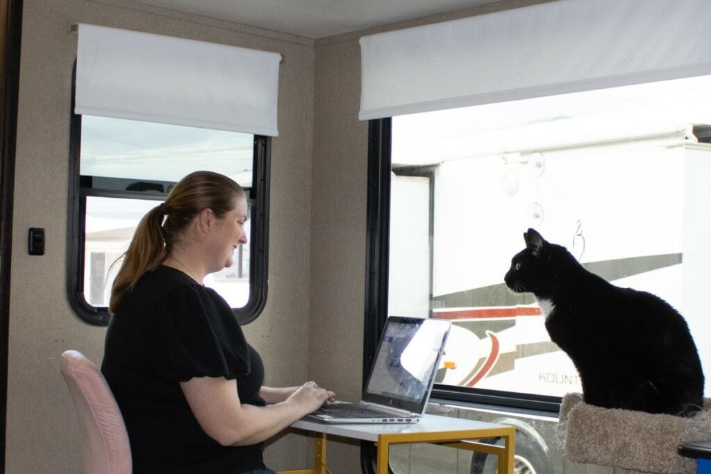 Digital nomad using laptop and internet from RV desk. Cat beside woman