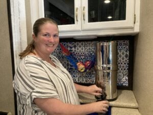 Woman using a water filter to pour water while standing in an RV kitchen. 