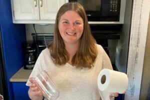 Woman inside RV holding empty jar and a roll of toilet paper.