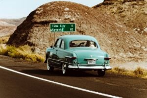 Old car pulled over in front of sign with mileage to next town.