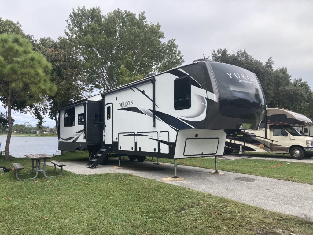 Fifth wheel RV parked in waterfront campsite on lake.