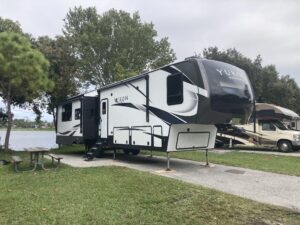 Fifth wheel RV parked in waterfront campsite on lake.