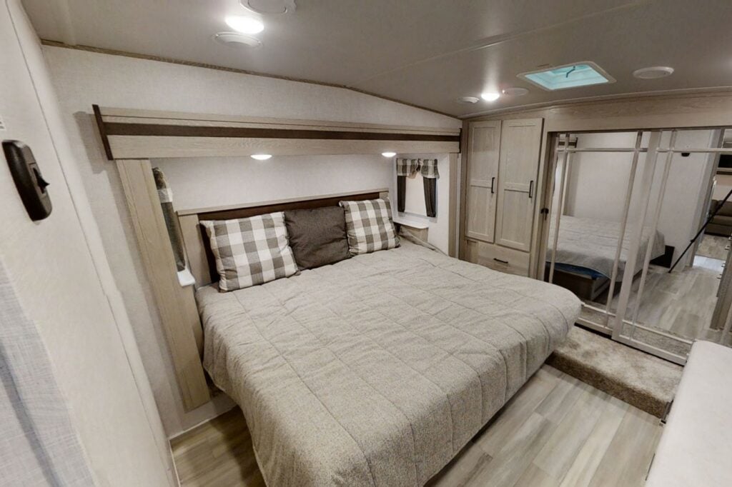 Bedroom inside a fifth wheel RV with light wood accents. 