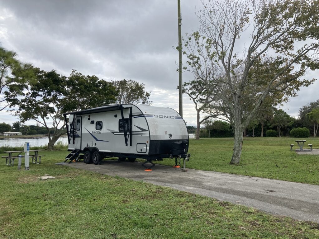 Small travel trailer RV parked on lake for cheap RVing trip.