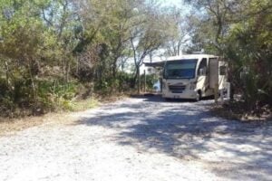 Class A RV parked on Florida state park campsite surrounded by trees with water in background.