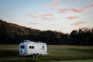 Oliver fiberglass camper parked in empty field in front of trees and dusk sky.