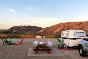 Fiberglass camper at campsite with chairs and fire pit.