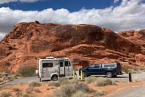 Fiberglass camper and pickup truck parked in front of red rock.