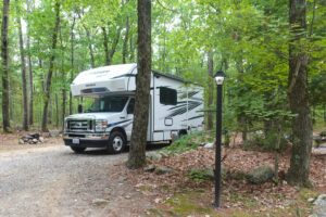 Class C RV parked in wooded campsite.