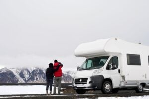 Couple beside RV on snowy road.