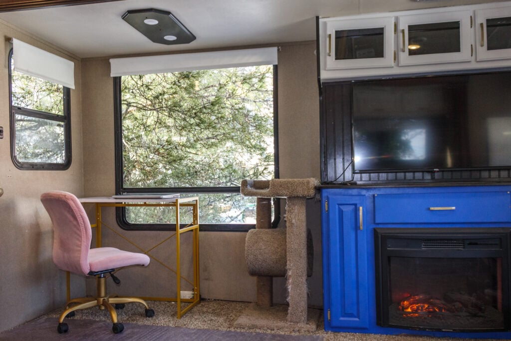 Interior of RV with desk, large window, TV and painted cabinets.