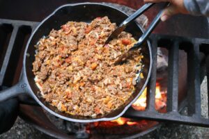 Taco filling cooking in cast iron pan over campfire.