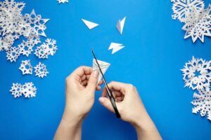 Hands cutting paper snowflakes with scissors.