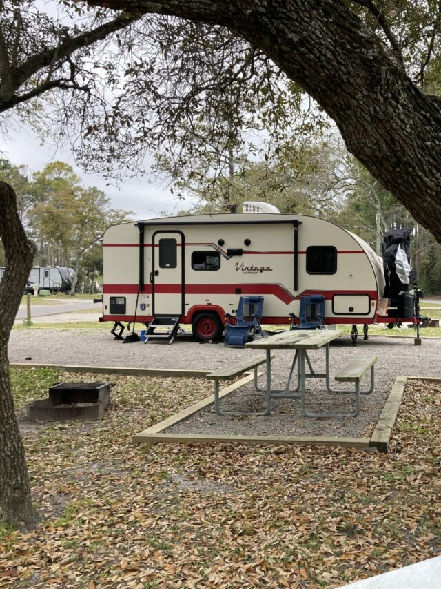 Vintage RV at pretty campsite with trees.