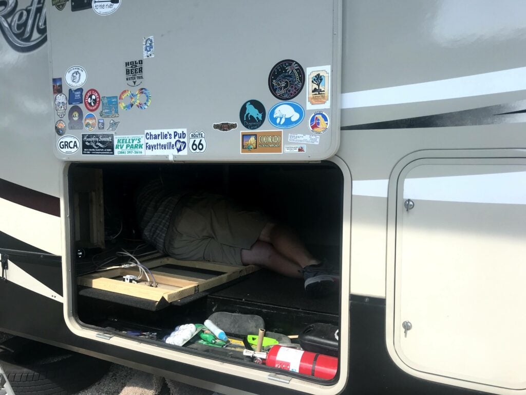 Man in RV basement storage area inspecting RV water heater.