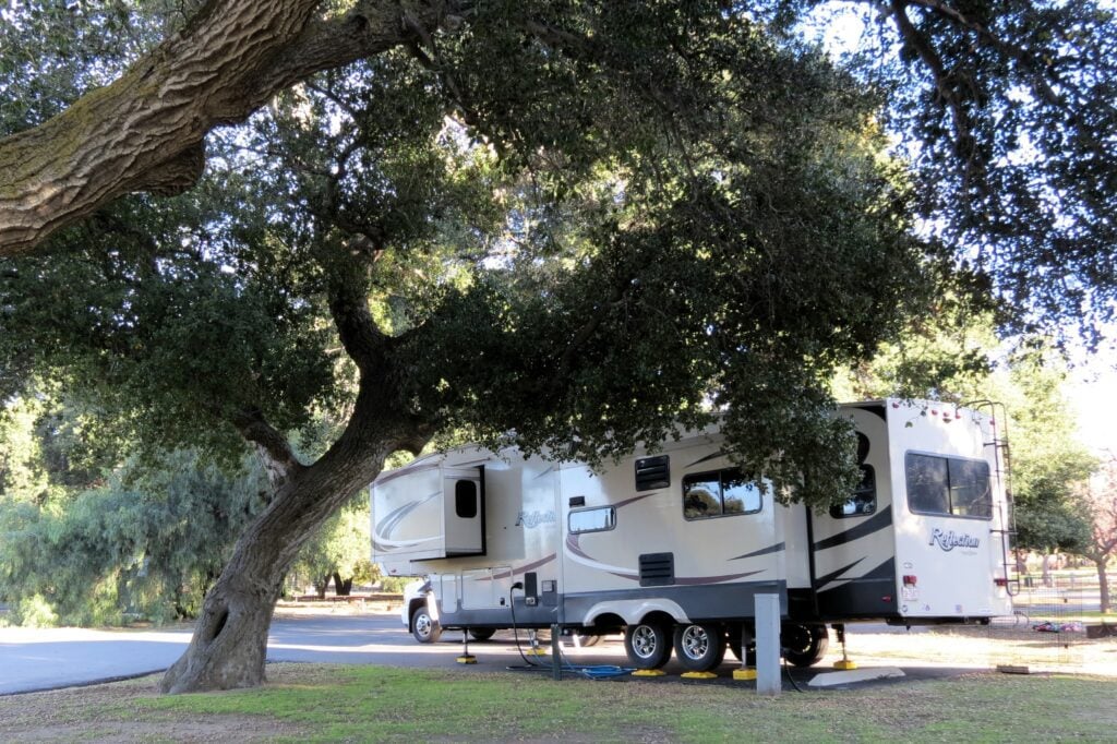 RV with power cord plugged in under large trees