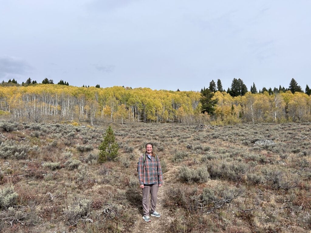 Woman hiking on trail with yellow Aspen trees.