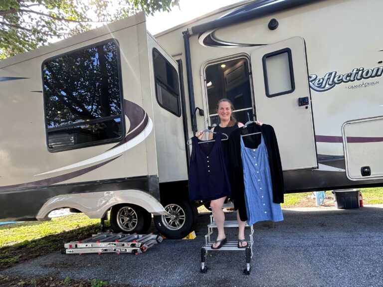 Woman standing on RV steps holding clothes on hangers.