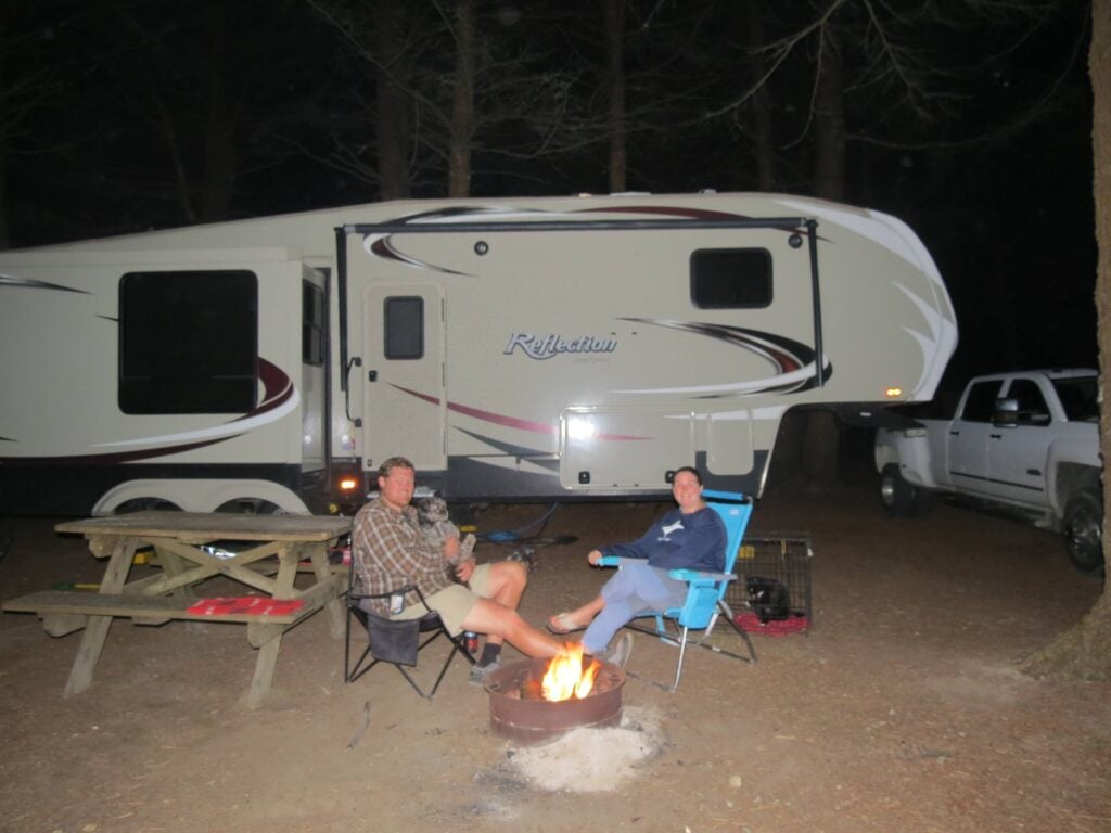 Couple and pets sitting outside RV at night.