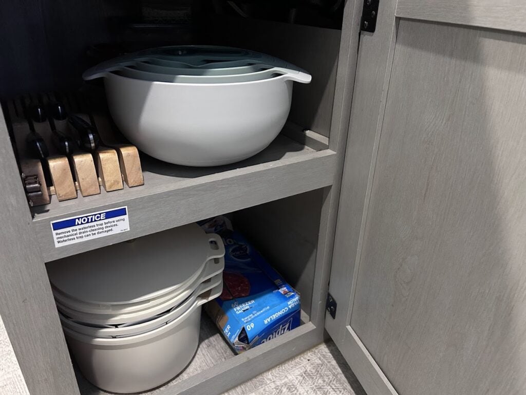 Knives, nested bowls and stacked cookware set in RV kitchen cabinet.