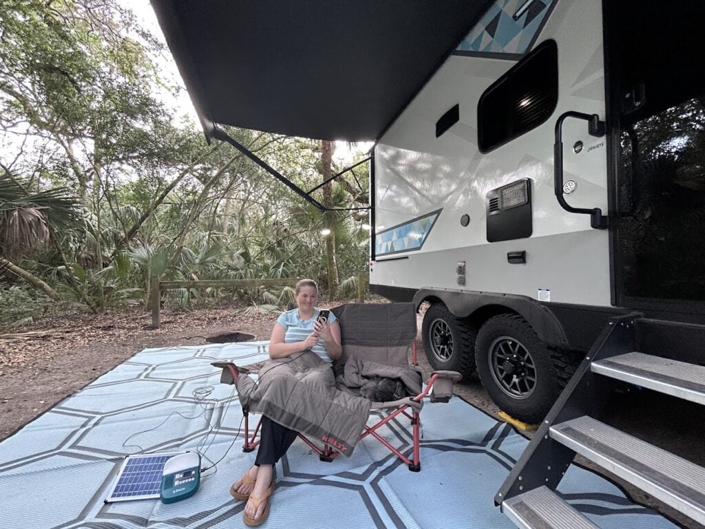 Woman sitting in camping loveseat and charging phone at RV campsite. 