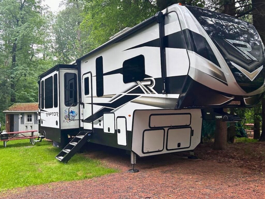 Fifth wheel RV with slide-out extened at wooded campsite.