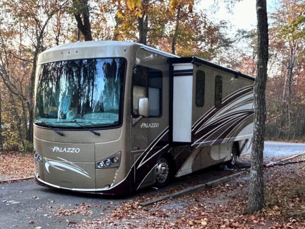 Beige motorhome at state park with topper over slide-out.
