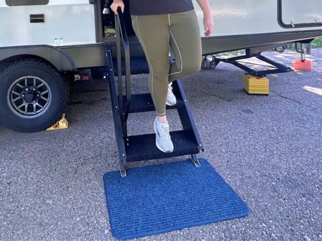 Feet walking down RV stairs with blue door mat below.